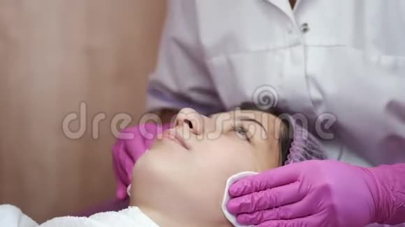 美容师用棉垫擦拭年轻女人的脸视频的预览图