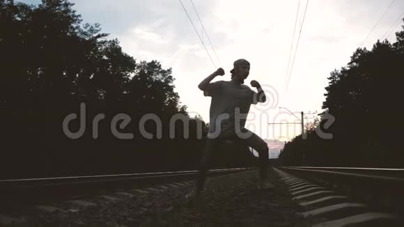 一个穿着破牛仔裤和t恤的人在铁路跑道上顶着太阳跳嘻哈舞视频的预览图
