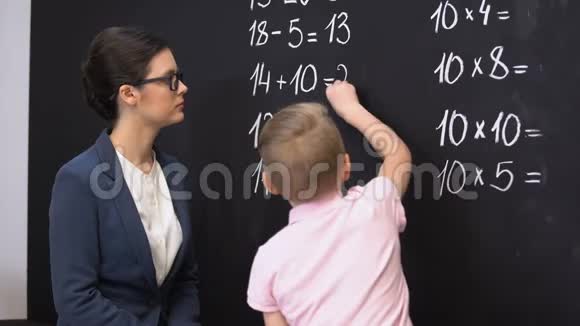 聪明的小学生在黑板上解决数学练习老师站在附近视频的预览图