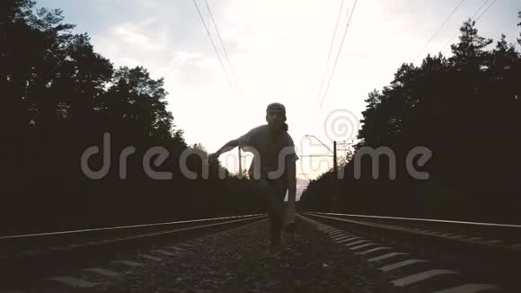 一个穿着破牛仔裤和t恤的男人在铁路跑道上靠太阳跳舞动作缓慢视频的预览图