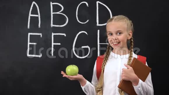 女孩拿着苹果靠近黑板健康的儿童零食字母书写视频的预览图