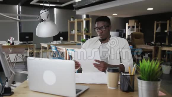 戴眼镜的非洲年轻人坐在办公室桌前拿着文件视频的预览图