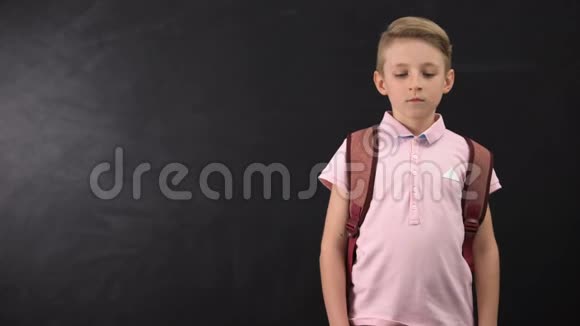 不高兴的疲惫的小学生站在黑板附近在学校里承受着过重的负担视频的预览图