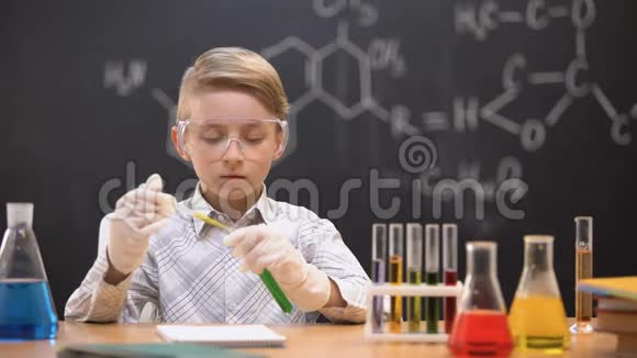 戴防护眼镜的男孩在管子里倒入化学物质检查反应视频的预览图