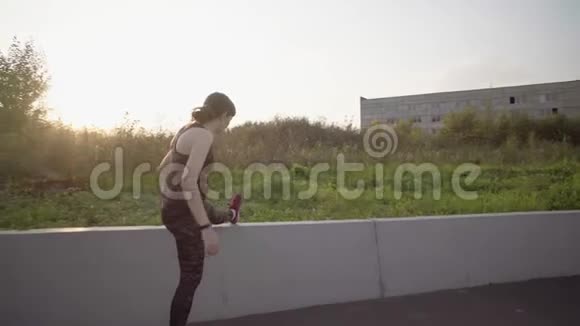 运动妇女伸腿把脚放在水泥栅栏上视频的预览图