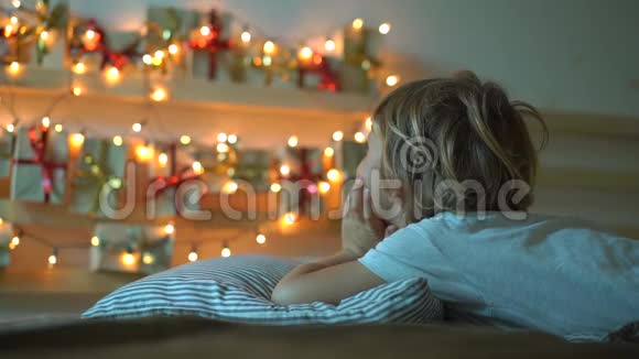 一个小男孩看着一张挂在床上的历法的慢镜头被圣诞灯光照亮得到的东西视频的预览图