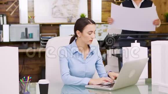 年轻的女建筑师在笔记本电脑上工作并与首席建造师交谈视频的预览图