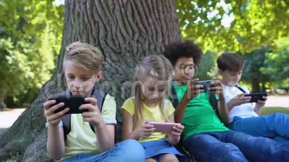 孩子们玩小玩意坐在公园的树下男孩在相机里微笑应用程序视频的预览图