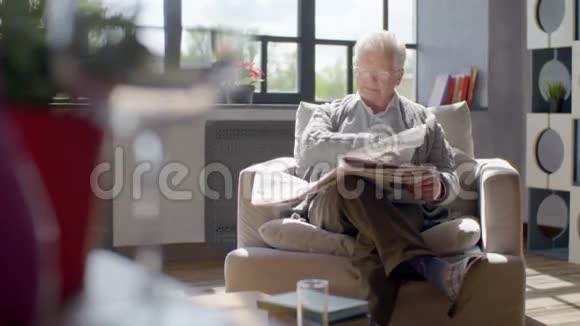 老人坐在椅子上在现代化的公寓里看报纸视频的预览图
