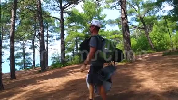 一位青年游客手里拿着背包走在森林小径上视频的预览图