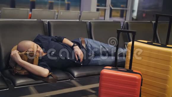 由于航班延误男人在机场过夜疲倦的人睡在等候室的座位上视频的预览图