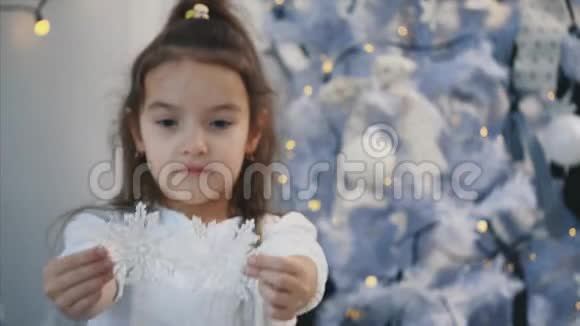 小女孩正在家里用银色的粉笔装饰一棵圣诞树并把它们拿给相机看视频的预览图