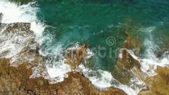 带石头和绿松石海波的悬崖海岸线的鸟瞰图垂直的无人机视频的预览图