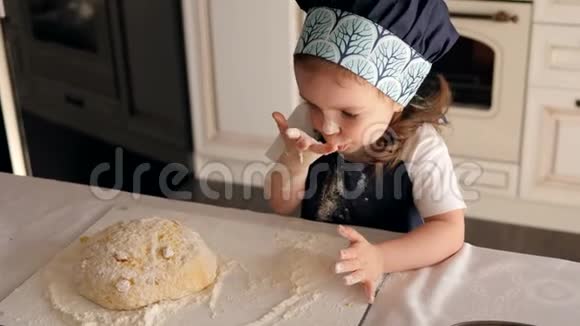 涂满面粉的可爱的小女孩在厨房里用面团舔她的手指视频的预览图