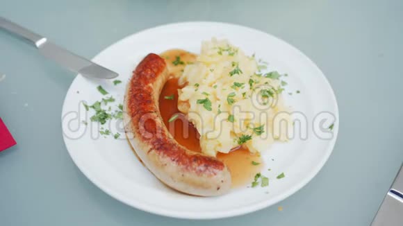 传统的德国菜盘烤香肠和白盘上的红烧白菜女人手拿刀叉视频的预览图