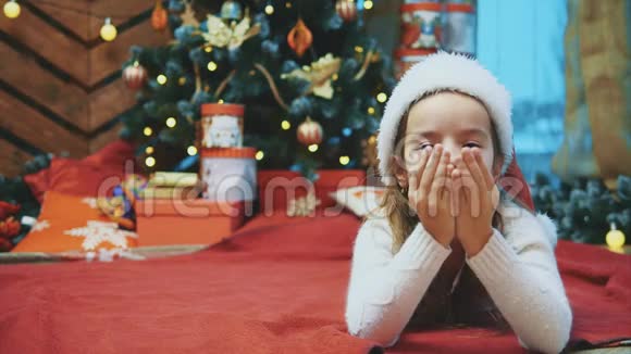 小女孩送空气亲吻花时间在圣诞树附近期待圣诞老人和礼物在圣诞节视频的预览图