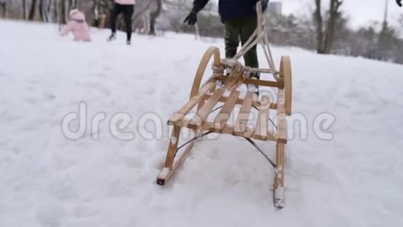 穿暖和衣服的可爱男孩在下雪的冬天拉木雪橇小男孩在公园里下雪跟踪视频的预览图