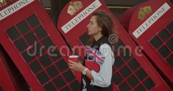 漂亮的女孩走在红色英国手机的背景上喝咖啡观光视频的预览图