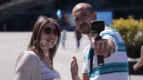 在城市水族馆附近的一个广场上男性和女性的视频博主们用相机自己拍照视频的预览图