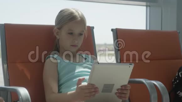 可爱的小女孩在机场用平板电脑等待他们的航班带着孩子出国旅行视频的预览图