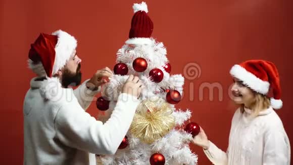 年轻夫妇戴着顶帽子用红色背景装饰圣诞树背景恋爱中的情侣新年视频的预览图