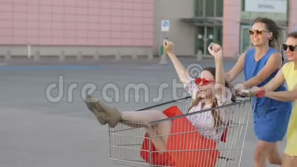 夏天三个戴太阳镜的漂亮女孩在超市下面的购物车里玩得很开心视频的预览图
