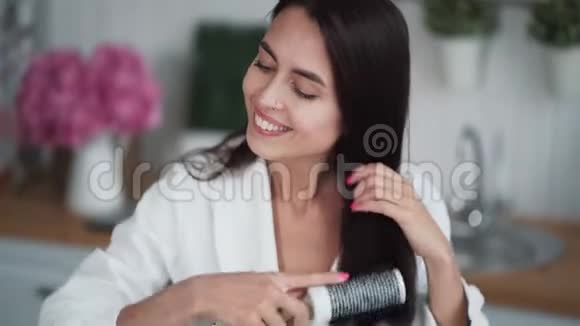 身着白色浴袍的年轻女子用梳子梳头看着镜头微笑着视频的预览图