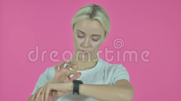 年轻女性在智能手表粉色背景上的浏览应用视频的预览图