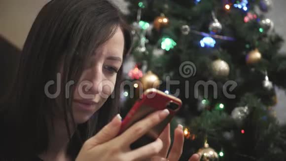 年轻女孩选择礼物在智能手机上而躺在地板上圣诞节视频的预览图