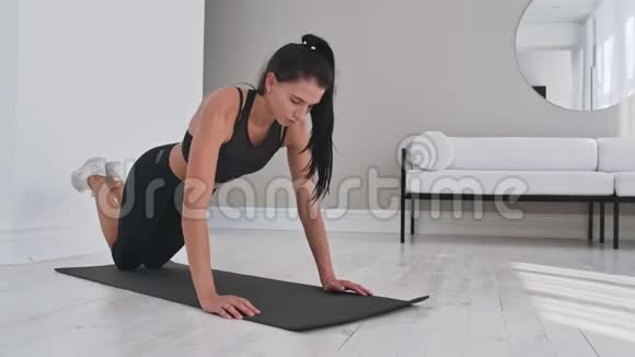 年轻性感的黑发女人穿着运动服在家里跪在地毯上做俯卧撑视频的预览图