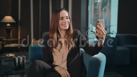 在酒店休息室在线使用智能手机视频通话的快乐女人视频的预览图