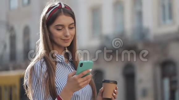年轻漂亮的女孩用她的智能手机站在老街上穿着带条纹的蓝色微笑视频的预览图