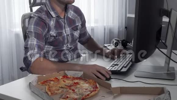 一个英俊的男人在电脑上吃美味的披萨视频的预览图