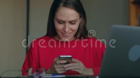 穿红色运动衫的女学生在家里的工作场所使用智能手机视频的预览图