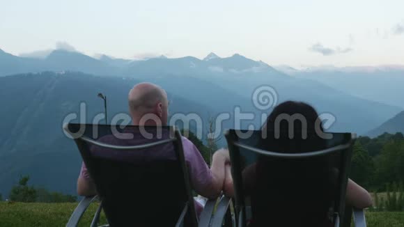 幸福的夫妻正在山上休息坐在阳光下俯瞰着群山绿树成荫视频的预览图