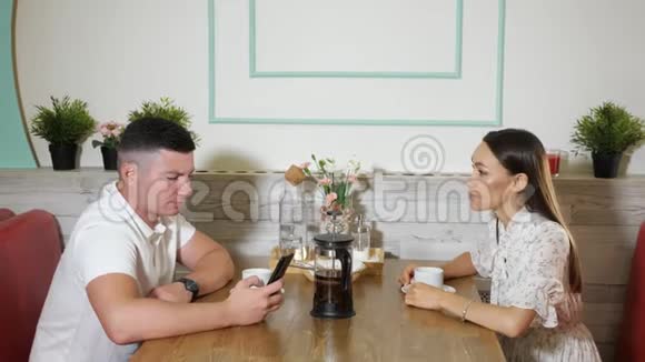 女孩与使用智能手机的男人在舒适的咖啡馆里聊天视频的预览图
