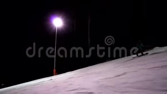 女性滑雪者独自沿着滑雪道快速骑行配有照明的滑雪道女孩们在晚上玩得开心视频的预览图