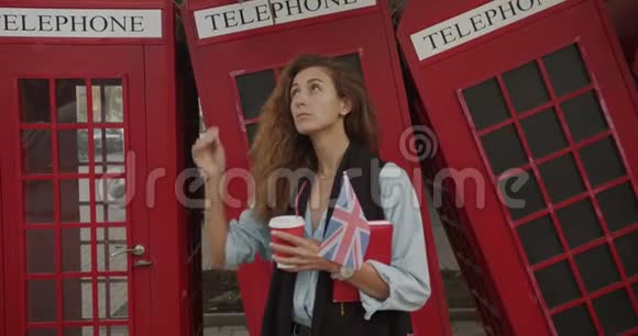 漂亮的女孩走在红色英国手机的背景上喝咖啡观光视频的预览图