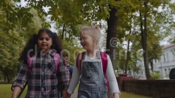 三个带背包的朋友要去上学混合种族的学生在公园里牵手行走视频的预览图