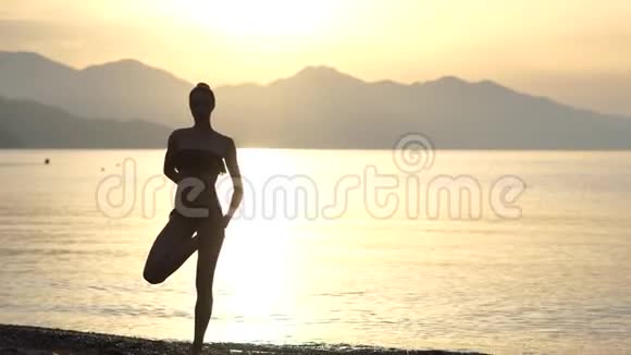 4K日出时在海滨做瑜伽姿势的优雅女性剪影视频的预览图