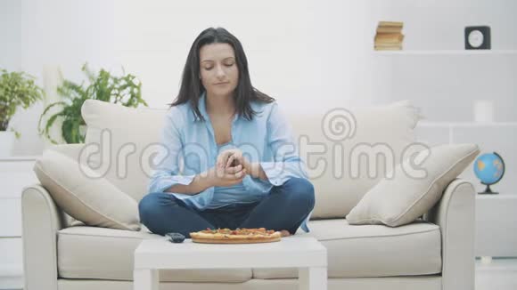 慢点一个年轻的女人正在打开电视节目而坐在沙发上她在吃披萨好吃好吃4K视频的预览图