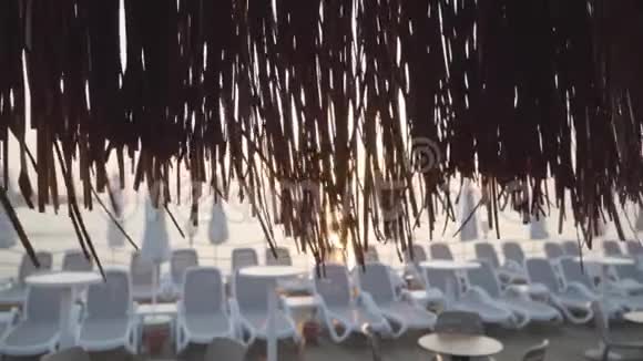 阳光透过稻草伞照射在东部海滩上阳光明媚的沙滩背景是白色的日光浴床冷静视频的预览图
