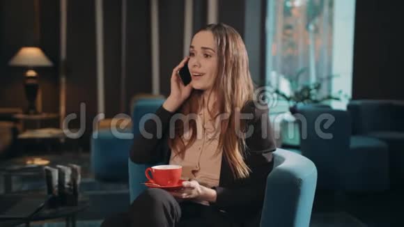 微笑的女人在酒店休息室打电话商务女性会说话智能手机视频的预览图