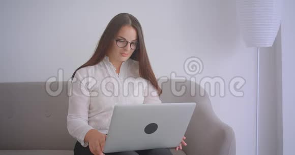 戴眼镜的白种人女商人的特写肖像她在笔记本电脑上打了个视频电话坐在室内的沙发上视频的预览图