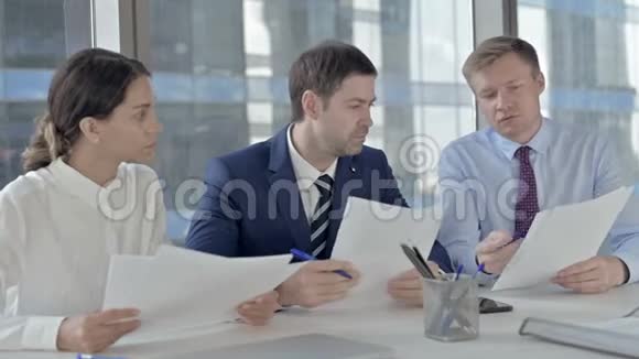 一位中年商人和他的助手在办公室桌上谈论文件视频的预览图