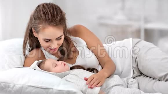 快乐迷人的年轻妈妈抚摸着熟睡的小宝宝在床上享受着早晨的中型镜头视频的预览图