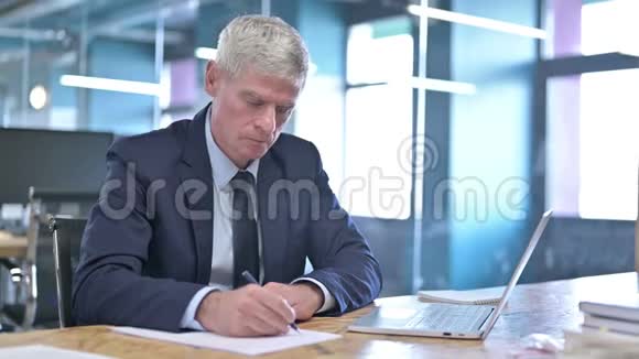 办公室办公桌上的中年商务人员书写笔记视频的预览图