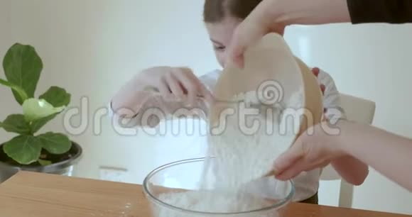 当妈妈把面粉倒进搅拌碗里时做面包面团的小女孩开心地笑了视频的预览图