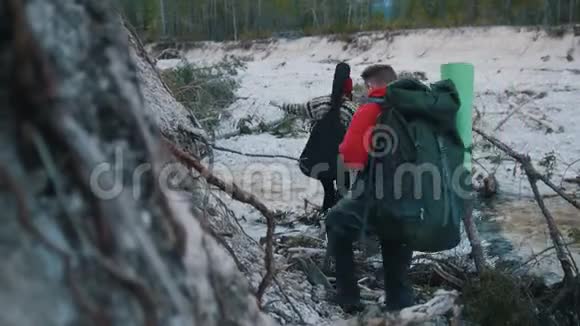 一个年轻的男女在森林的背景上背着背包和吉他在原木上穿过岩石河视频的预览图
