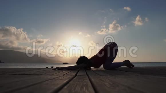 4K一个年轻女孩在日出时慢动作在海边做瑜伽练习视频的预览图